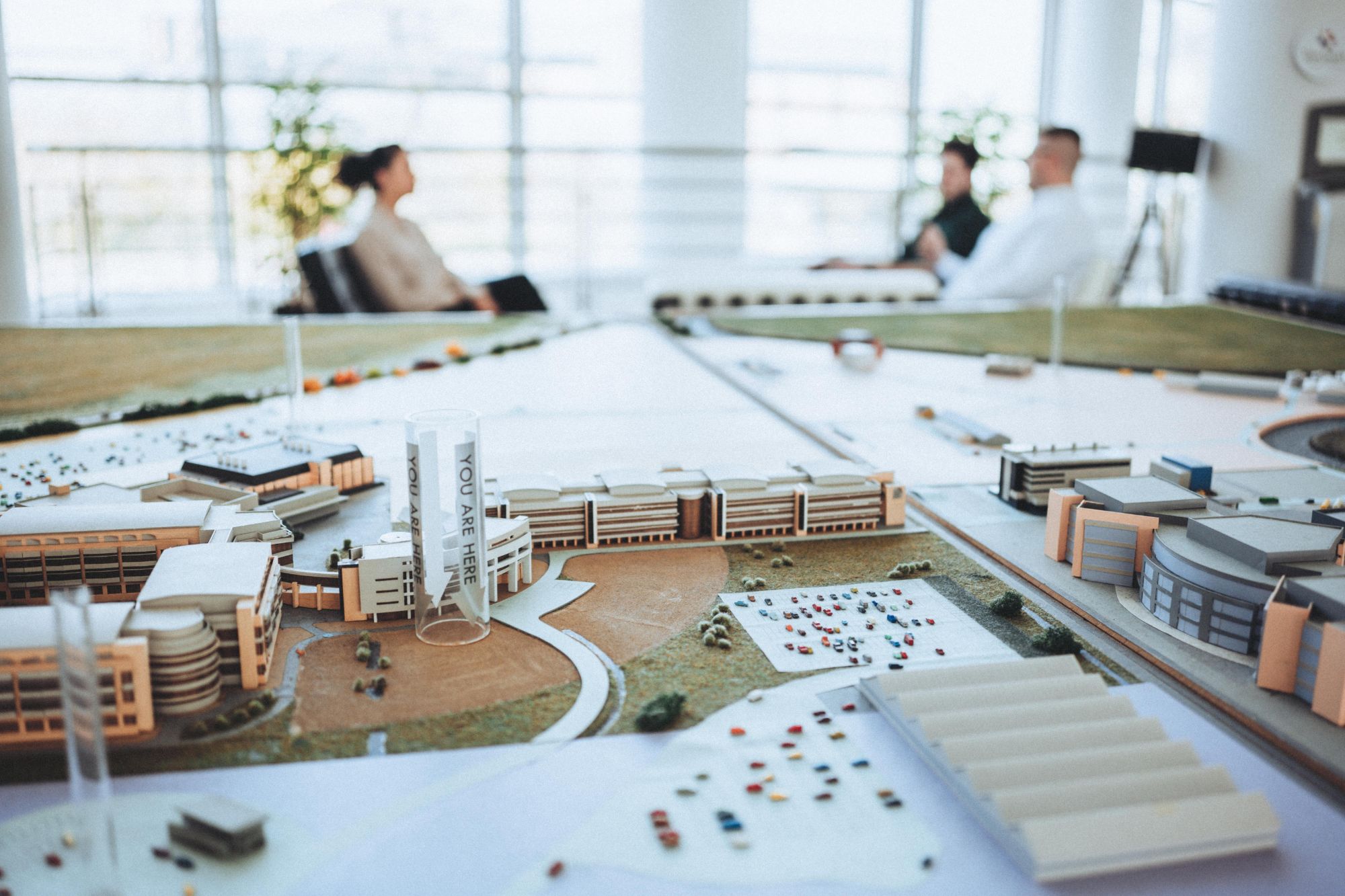 Architectural model of a business campus, with colleagues meeting in the bright office beyond